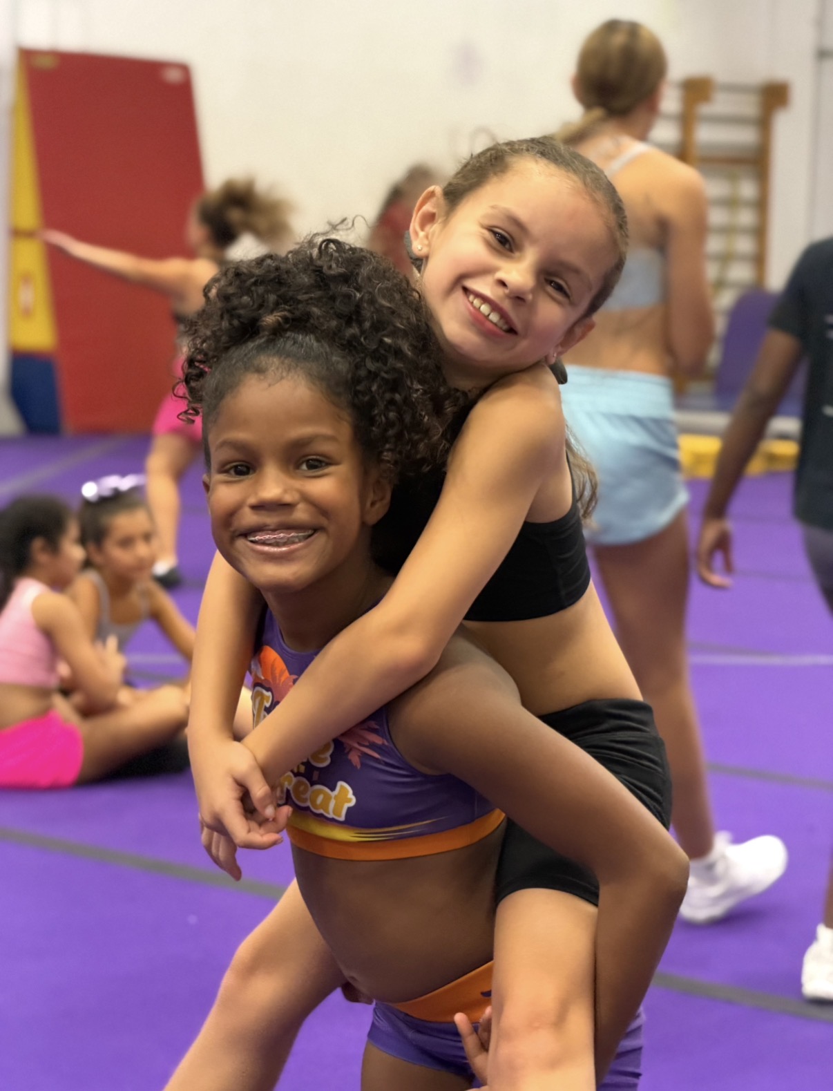 Two young F3T athletes smiling during a piggyback ride at practice